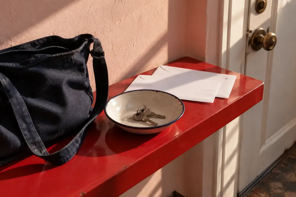 Llaves, sobres cerrados y una bolsa de tela descansan sobre una repisa roja junto a la puerta.