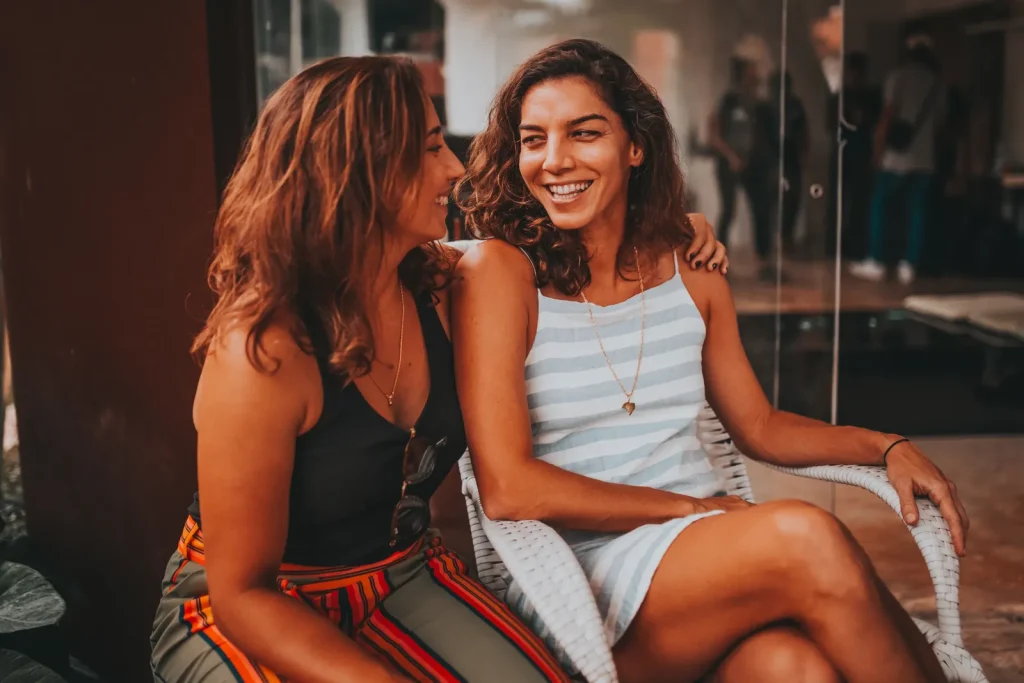 Dos mujeres jóvenes sentadas una junto a la otra ríen mientras conversan