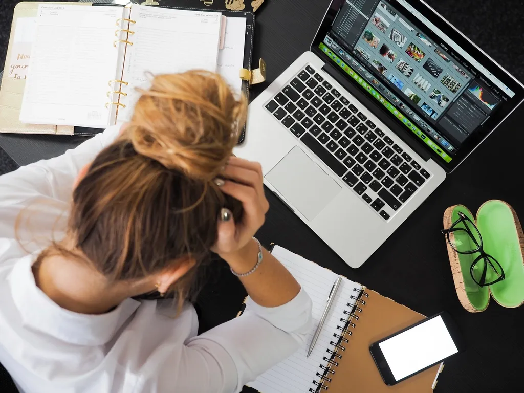 Mujer apoya la cabeza en sus manos frente a una computadora portátil y una agenda abierta