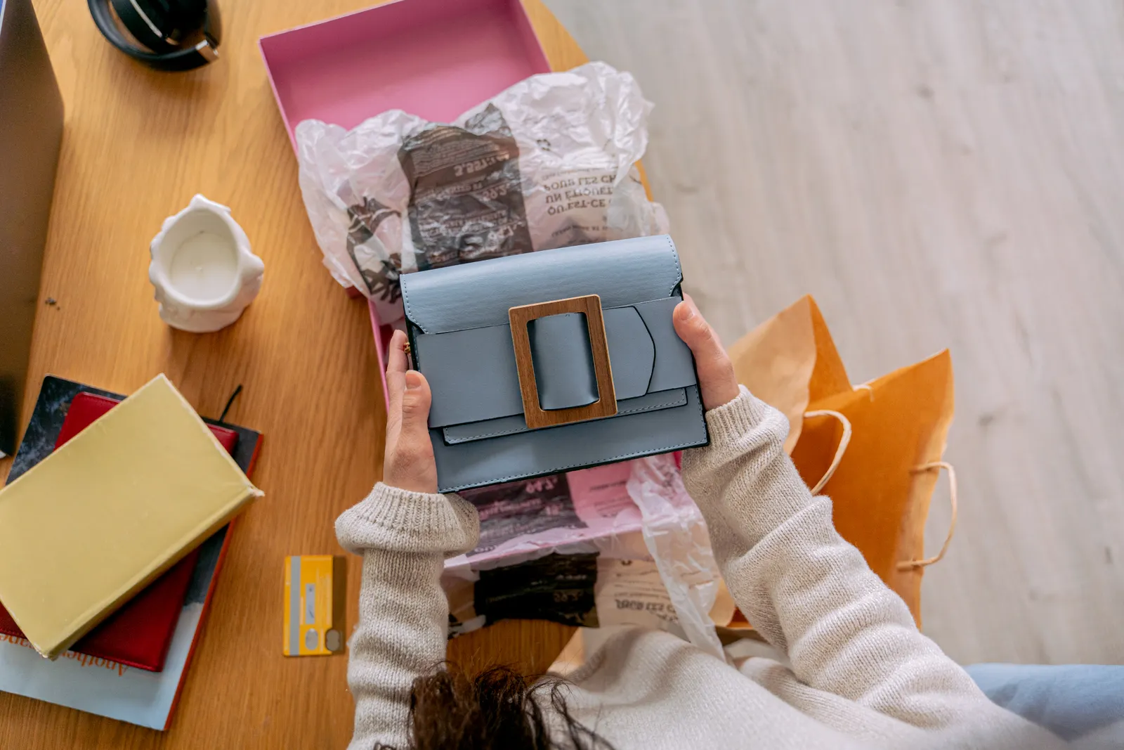 Manos sacan una bolsa de mano azul de su caja, rodeada de bolsas de compras y papel