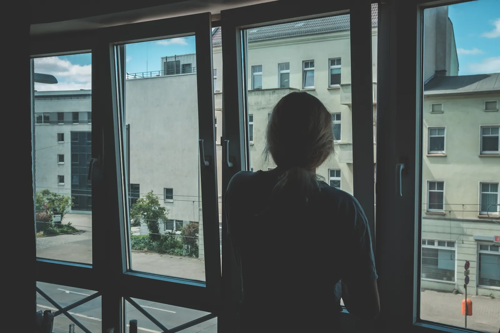 Mujer de espaldas mira por una ventana grande hacia los edificios de la ciudad