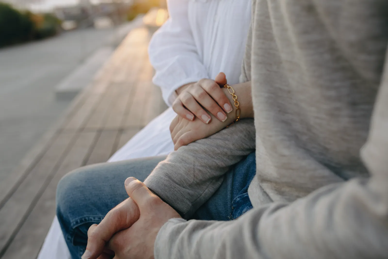 Primer plano de una pareja sentada en una banca, con una mano apoyada en el brazo de la otra persona