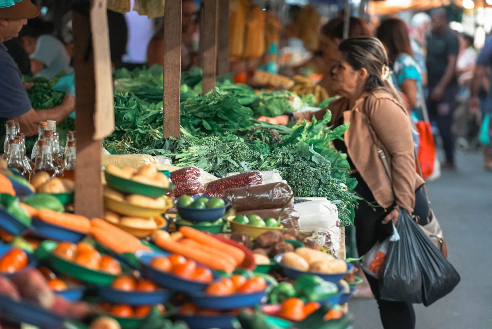 Puesto de mercado con zanahorias, pimientos y verduras frescas mientras una mujer hace sus compras