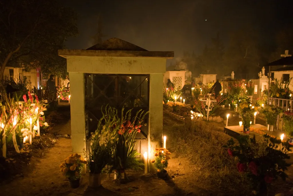 Panteón iluminado con velas y flores durante la noche de Día de Muertos