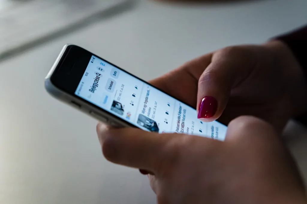Primer plano de unas manos con uñas pintadas que deslizan una red social en un celular