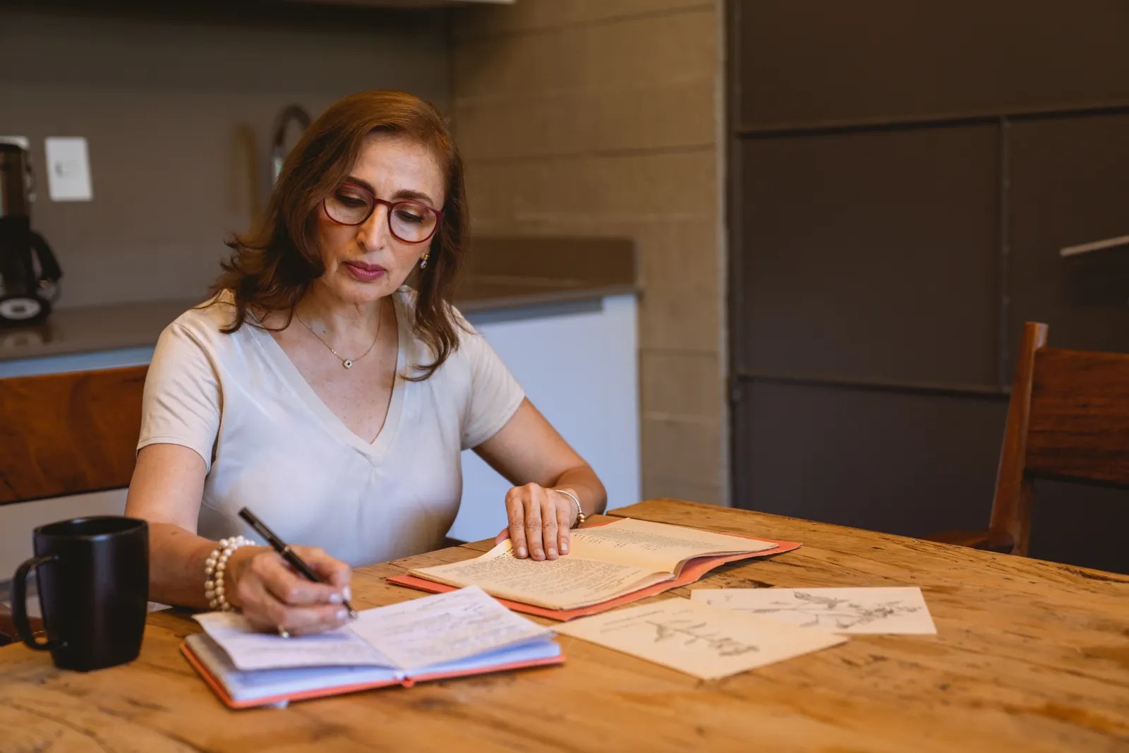 Mujer con lentes escribe notas en un cuaderno sobre una mesa de madera con libros