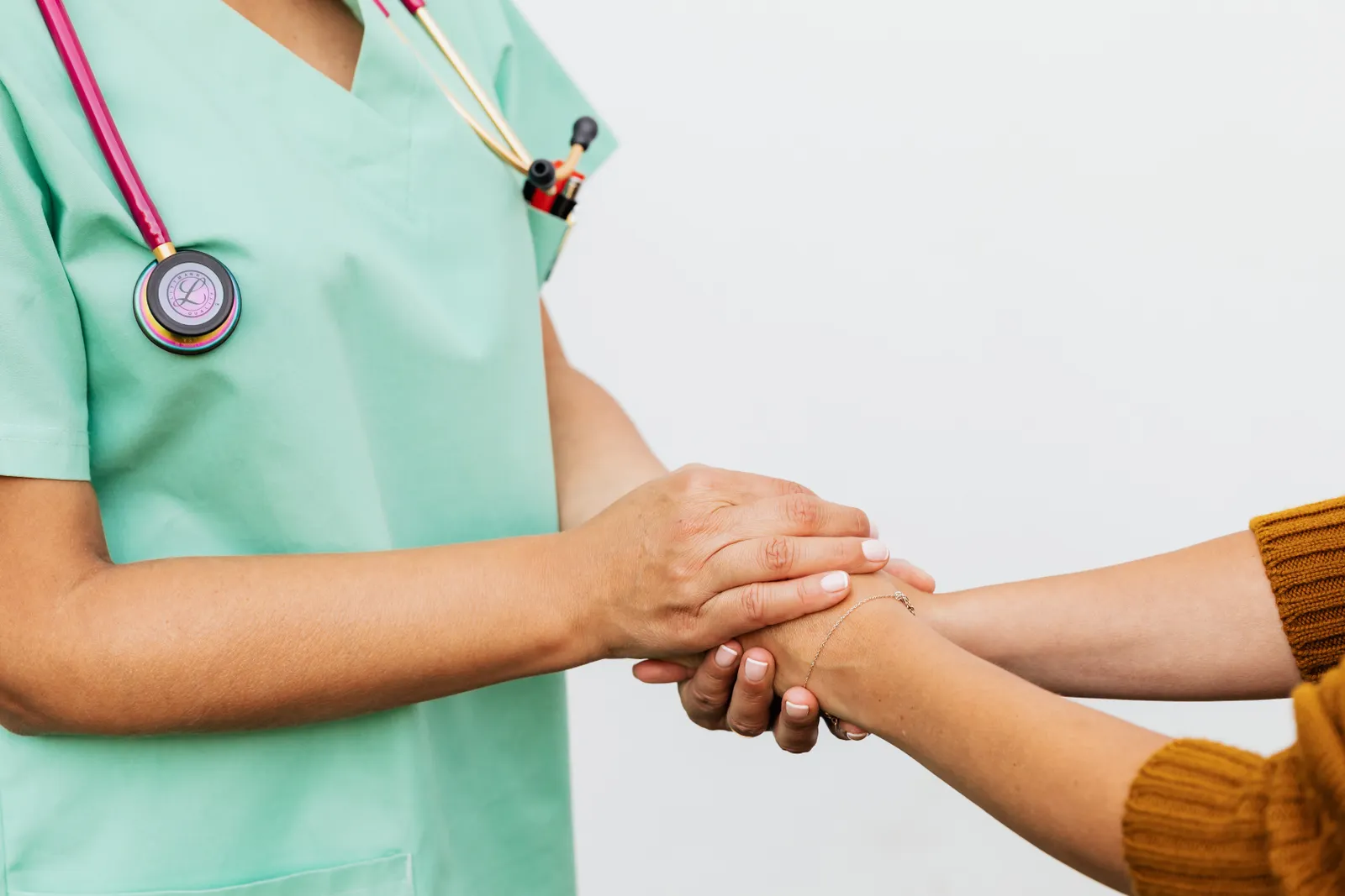 Una profesional de la salud con uniforme verde toma con apoyo las manos de una paciente