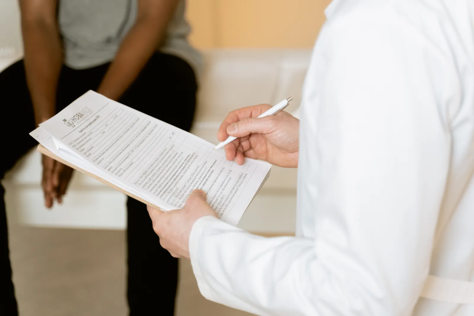 Profesional de la salud revisa un formulario mientras una paciente espera sentada