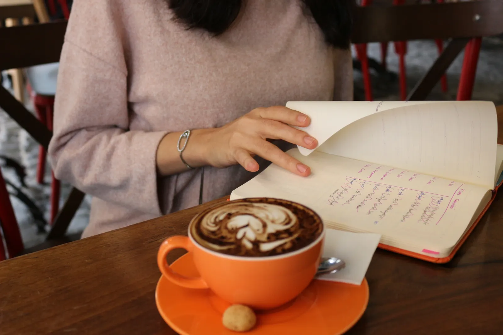 Mujer hojea un cuaderno escrito a mano junto a una taza de café con leche