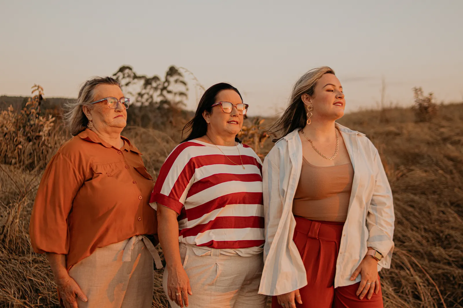 Tres mujeres de distintas edades posan juntas en un campo al atardecer