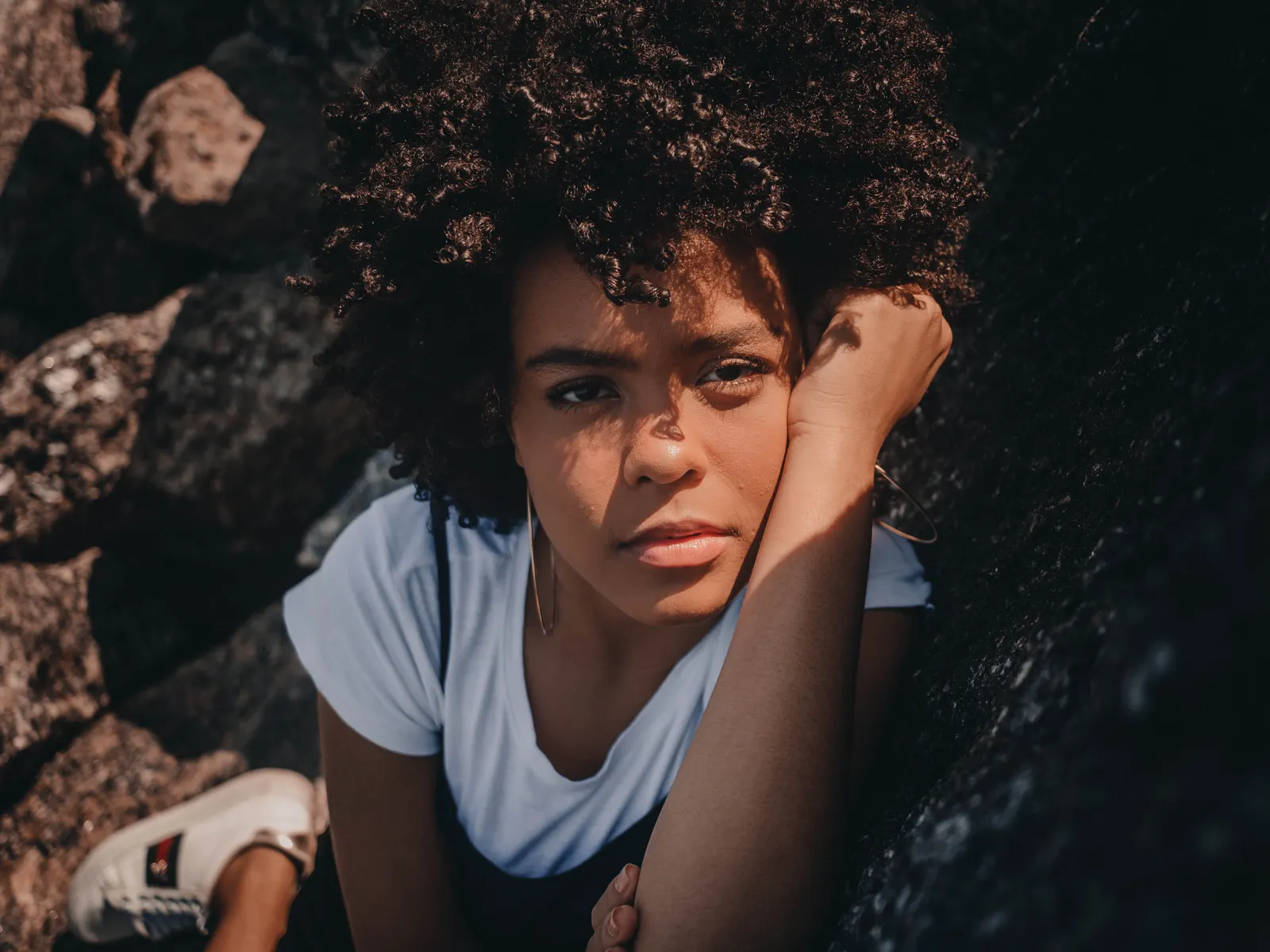 Mujer joven de cabello afro mira a la cámara con expresión seria, apoyada en una roca