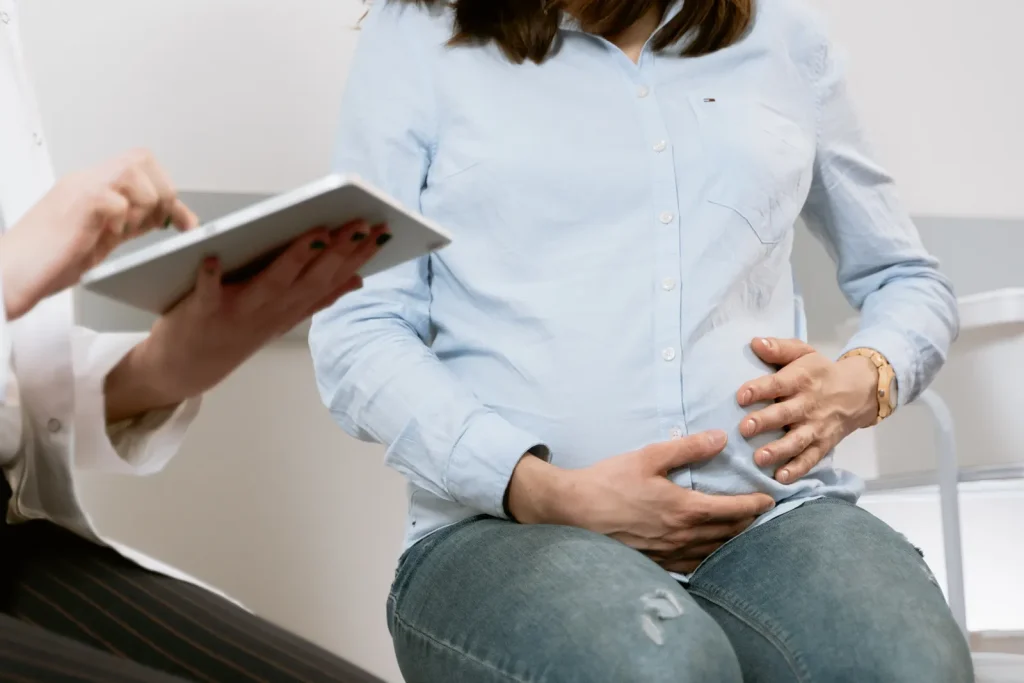 Mujer embarazada sentada con las manos sobre el vientre durante una consulta médica