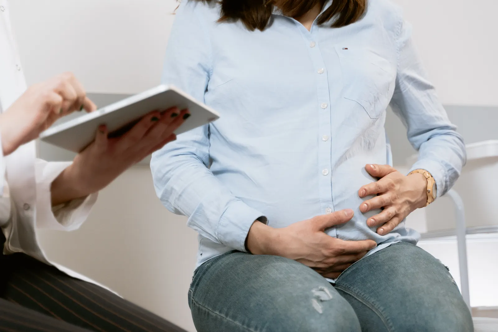 Mujer embarazada sentada con las manos sobre el vientre durante una consulta médica