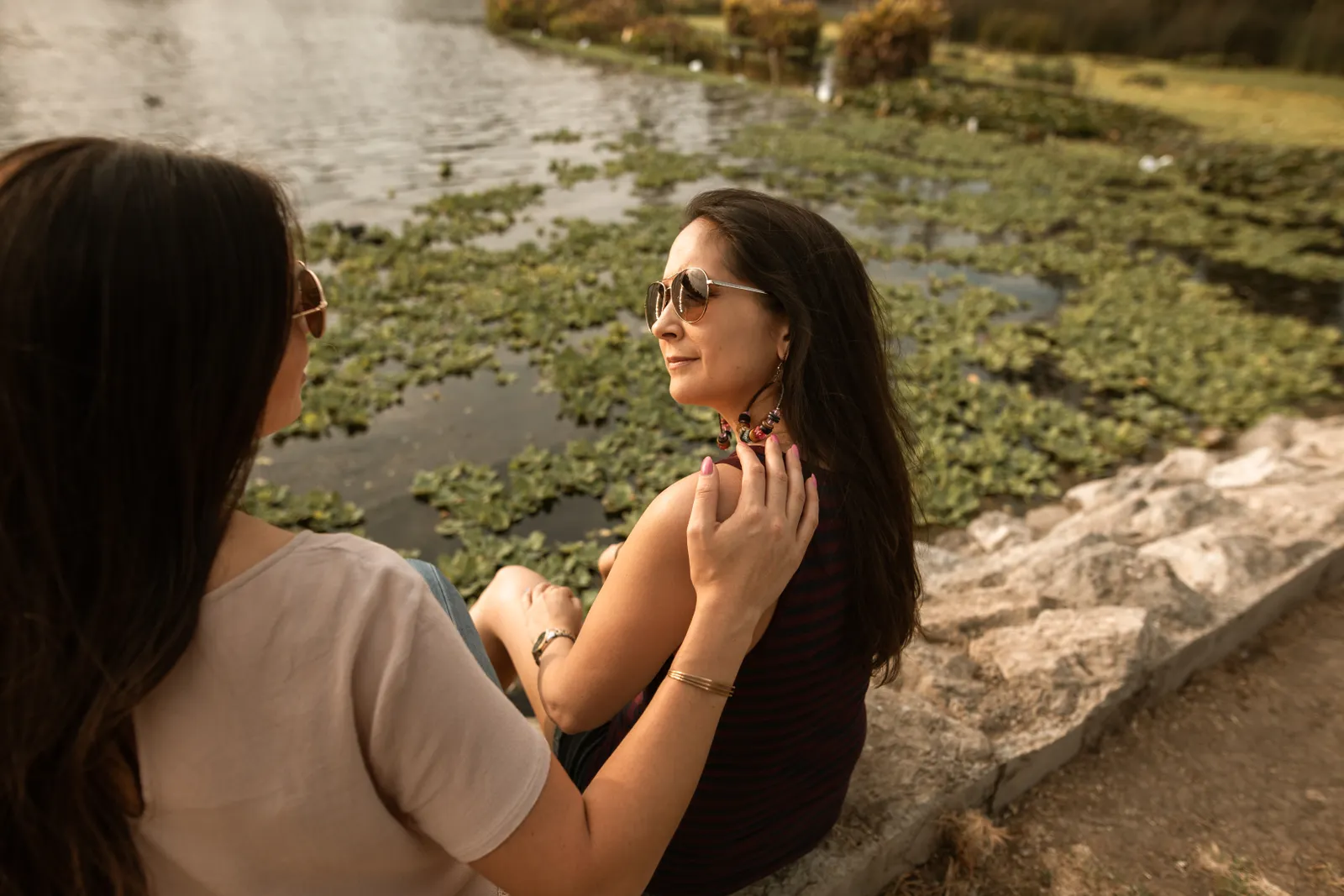 Dos mujeres conversan sentadas a la orilla de un lago en una tarde soleada