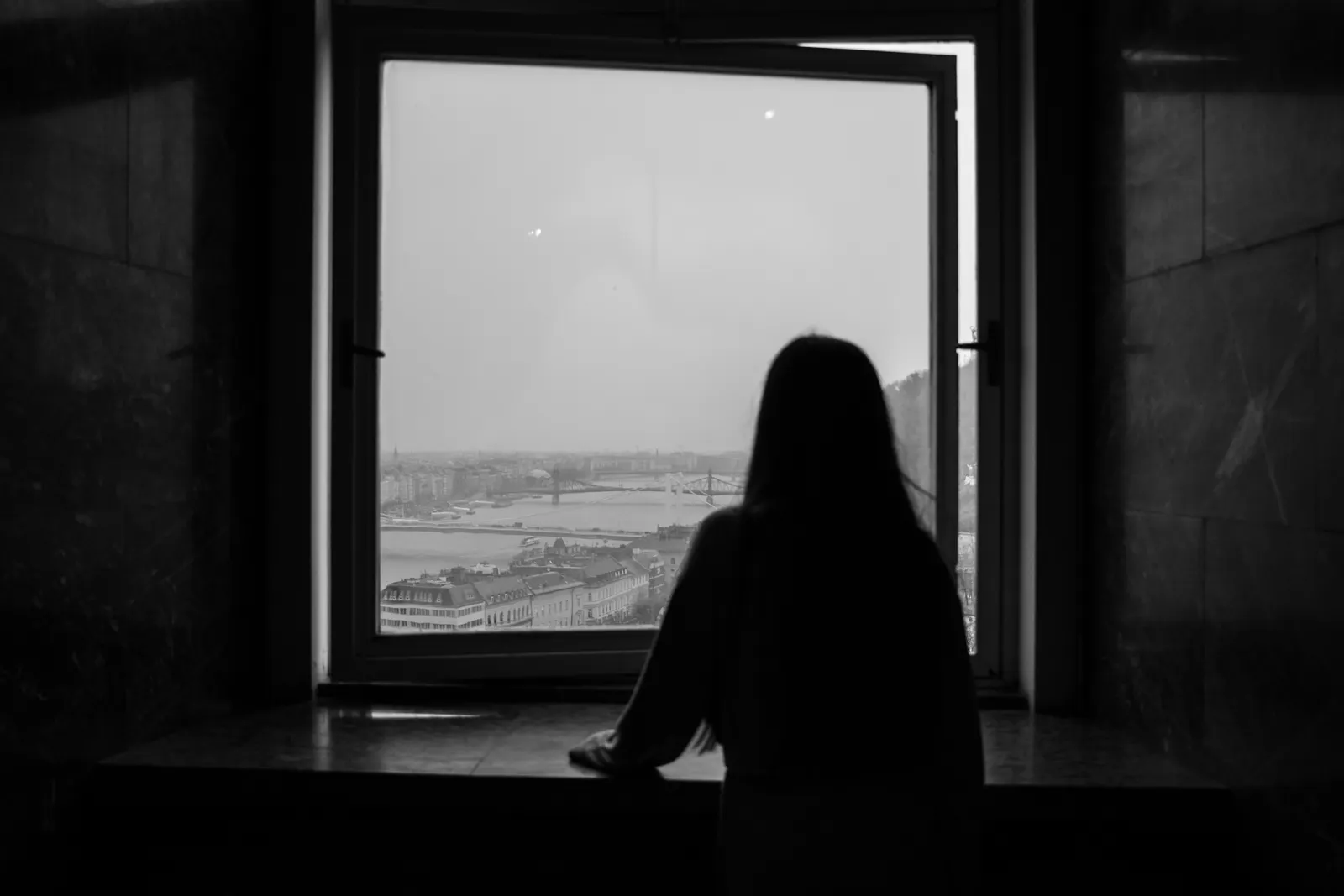 Silueta de una mujer sentada frente a una ventana en blanco y negro