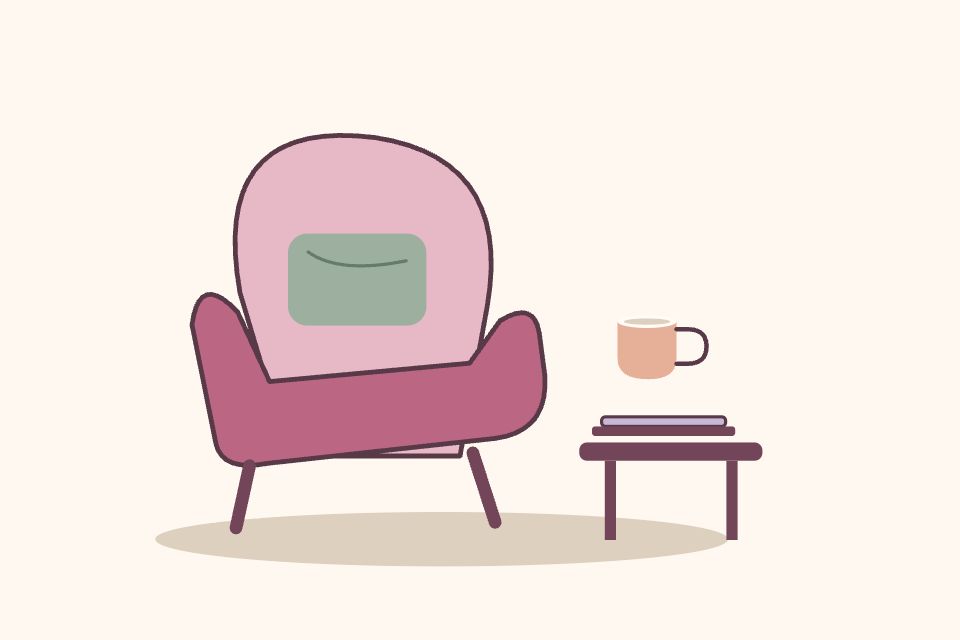 Un sillón rosa con cojín verde junto a una taza y una computadora cerrada.