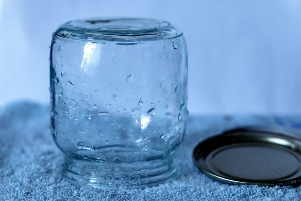 Frasco de vidrio transparente con su tapa de metal sobre una tela azul.