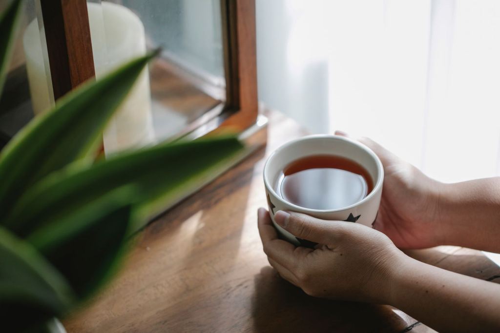 Manos sostienen una taza de té de hierbas junto a una ventana.