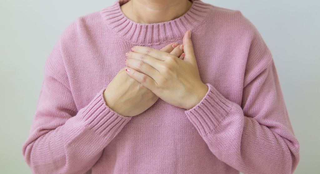 Mujer con suéter rosa coloca las manos sobre el pecho en una pausa para respirar.