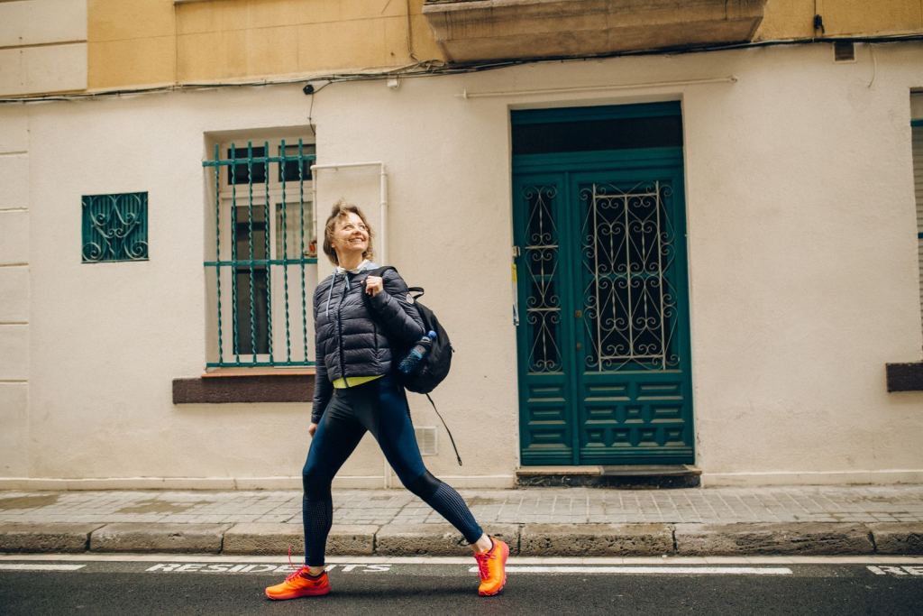 Mujer sonriente camina con paso rápido por una calle soleada.