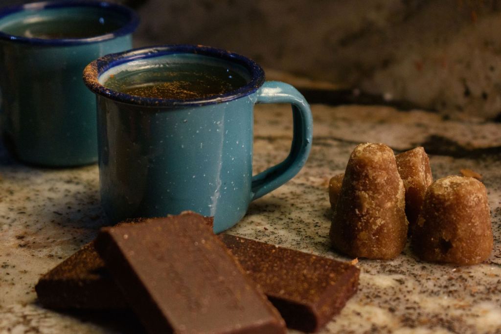 Chocolate caliente en una taza de peltre azul junto a piloncillo y tablillas de chocolate.