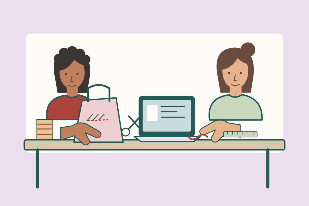 Dos amigas trabajan en una mesa con una bolsa de tela, herramientas de costura y una computadora abierta.