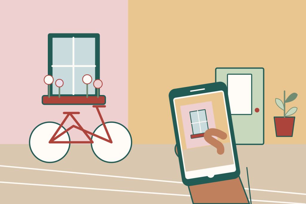 Una mano sostiene un celular para fotografiar una fachada con flores, una ventana y una bicicleta en una calle tranquila.