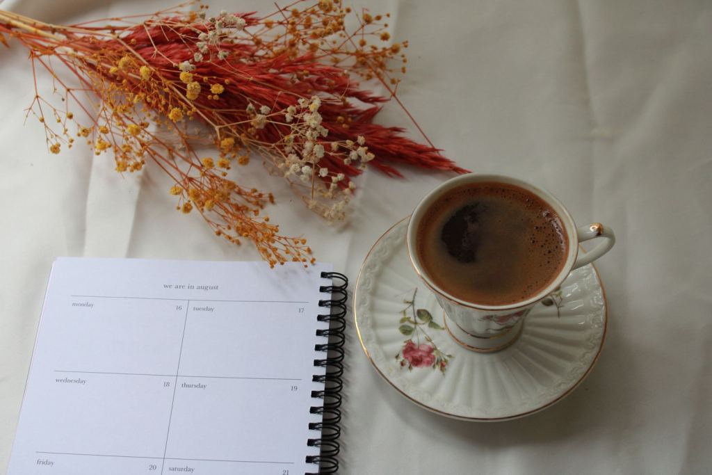 Agenda abierta junto a una taza de café y flores secas.