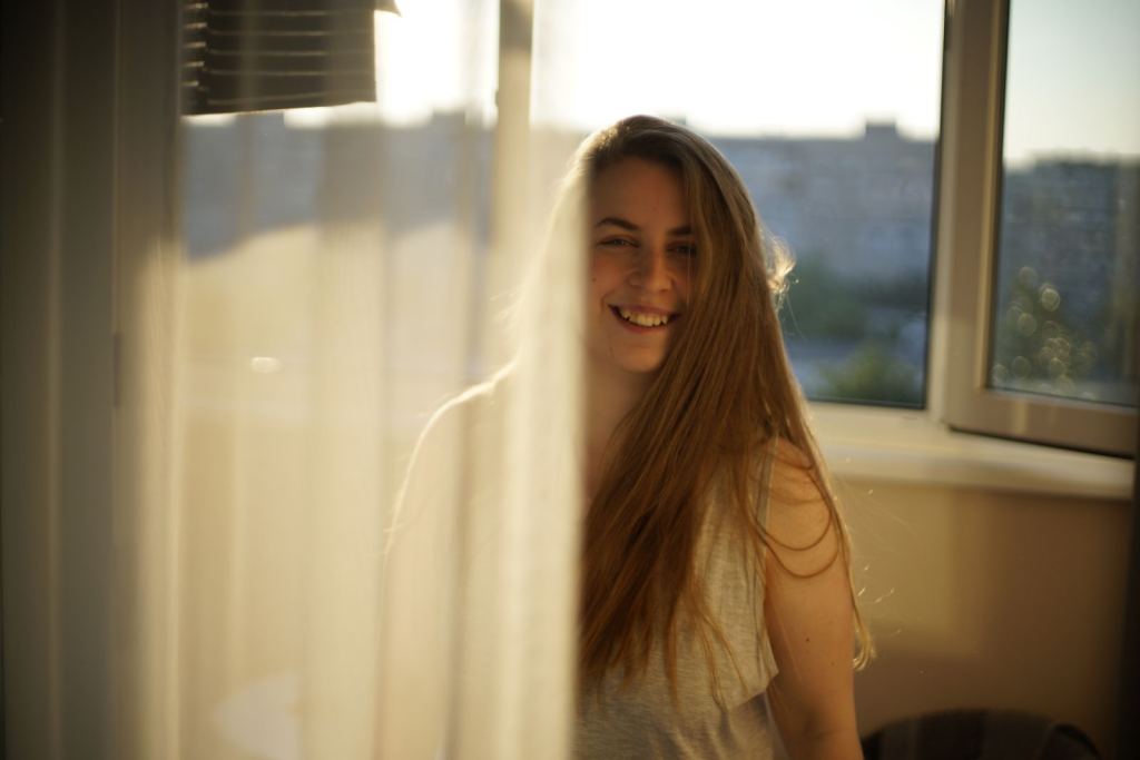 Mujer sonríe junto a una ventana mientras entra la luz del sol.