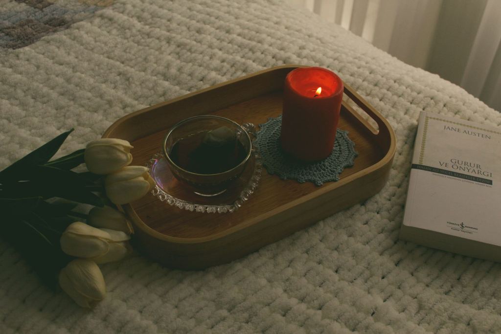 Bandeja junto a la cama con una vela encendida, una taza de té y un libro.