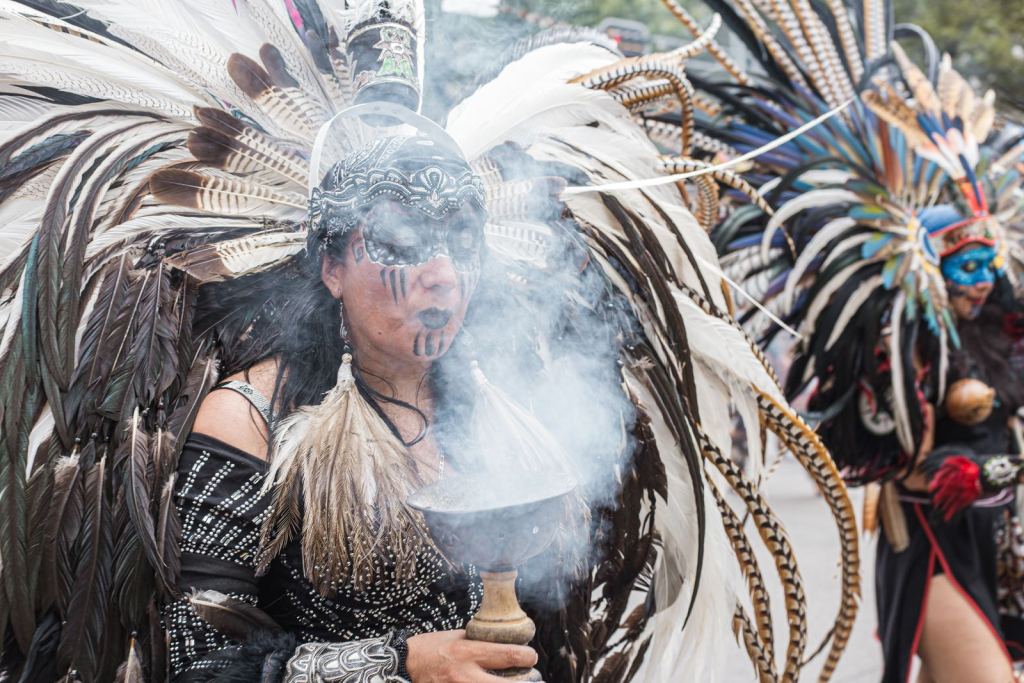 Danzante con penacho de plumas sostiene un sahumador con humo de copal en la Ciudad de México.
